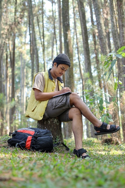 Young Asian man find an inspiration for writing a novel or journal surrounded pine trees at the fore