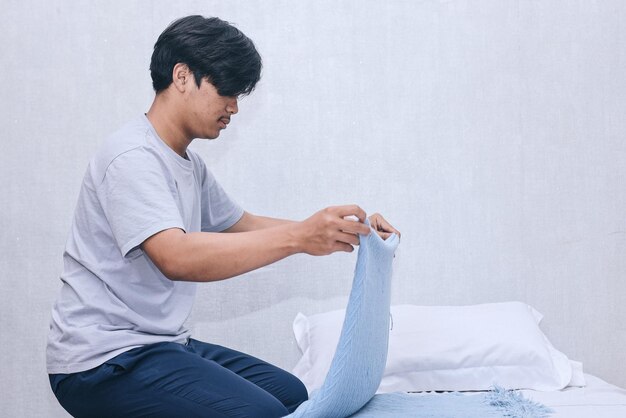 Young Asian man folding blanket after waking up from sleep Morning routine activity