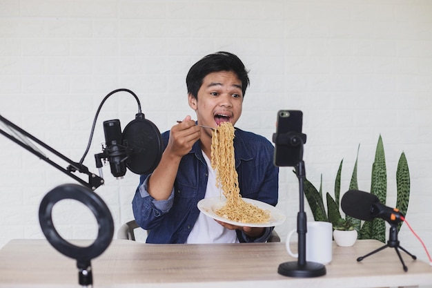 Young Asian man food blogger or vlogger showing and recording a live video of noodle