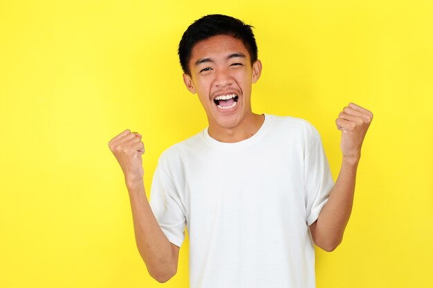 젊은 아시아 남자는 승리하는 제스처를 표현하는 행복하고 흥분합니다. 노란색 배경에서 성공하고 축하합니다.