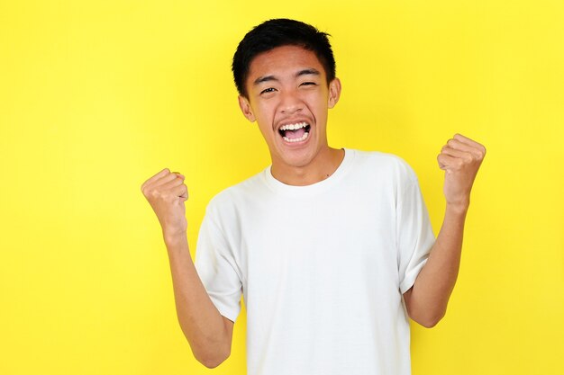 Young asian man happy and excited expressing winning gesture. Successful and celebrating on yellow background