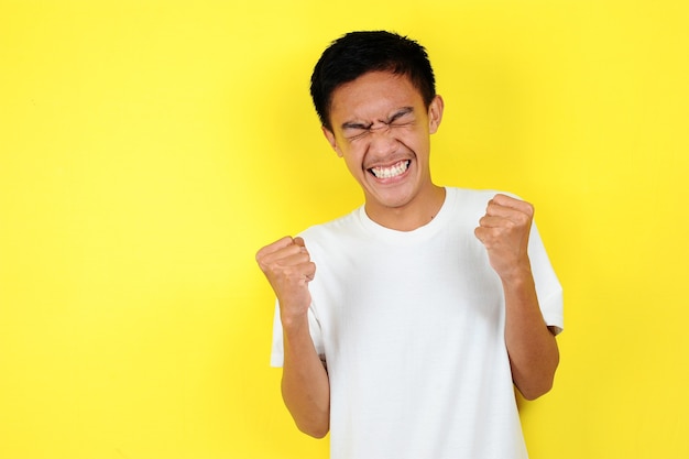 Young asian man happy and excited expressing winning gesture. Successful and celebrating on yellow background