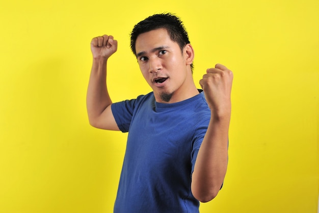 Young asian man happy and excited expressing winning gesture. Successful and celebrating on yellow background