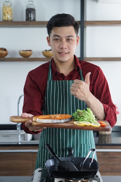 Giovane uomo asiatico felice con il suo pasto che cucina