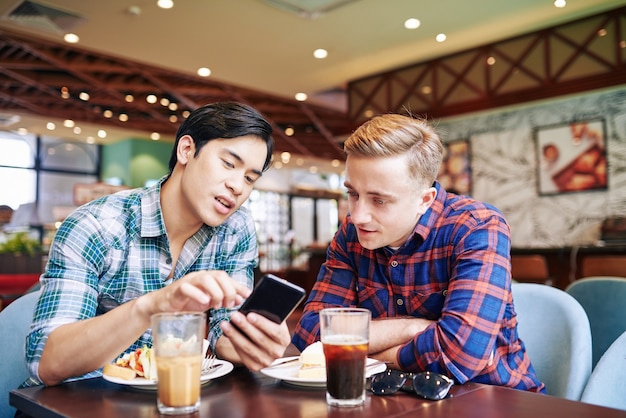 カフェで友人と昼食をとり、友人にスマートフォンで新しいモバイルアプリケーションを見せてアジアの若い男