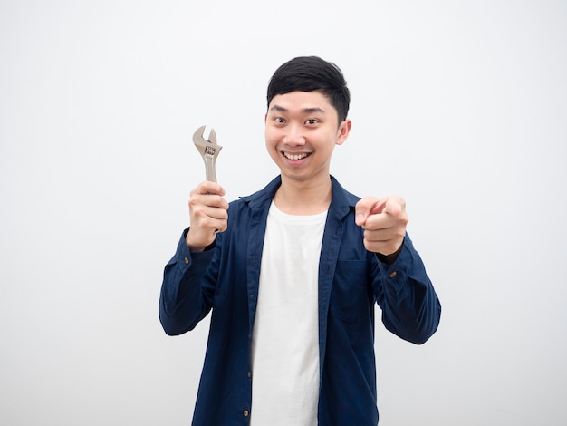 Young asian man holding adjustable wrench point finger at you with happy smile feeling cheerful