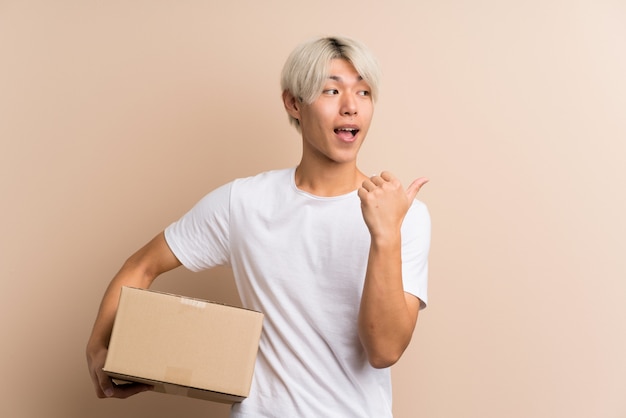 Young asian man holding a box to move it to another site and pointing side