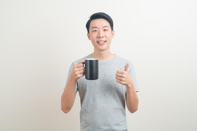 Giovane uomo asiatico che tiene la tazza di caffè con la faccia sorridente su sfondo bianco