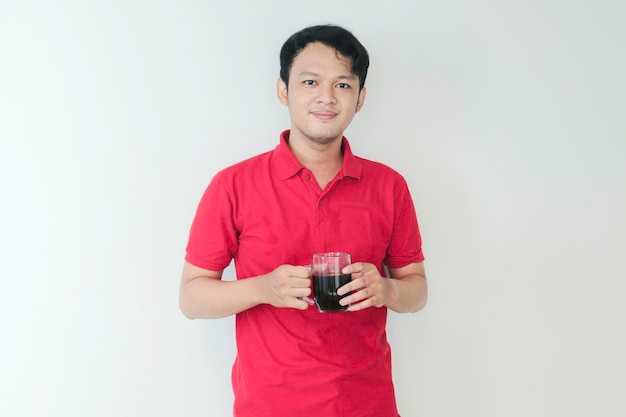 Молодой азиатский мужчина держит чашку кофе, стоящую на изолированном белом фоне, счастливую с широкой улыбкой