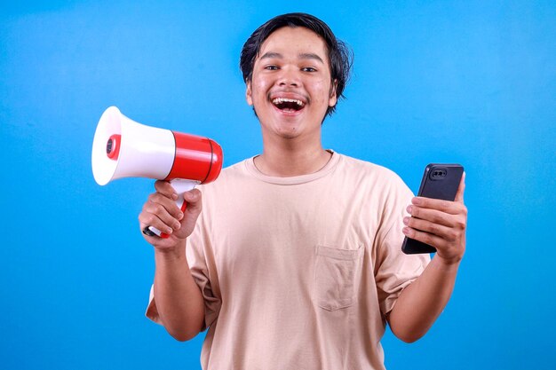 Young Asian man holding megaphones and smartphone while looking at camera with happy expression