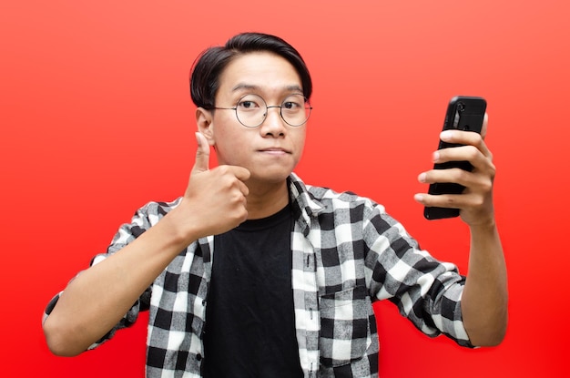 Young asian man holding phone in various expression sad, happy,\
shocked, angry isolated over red.