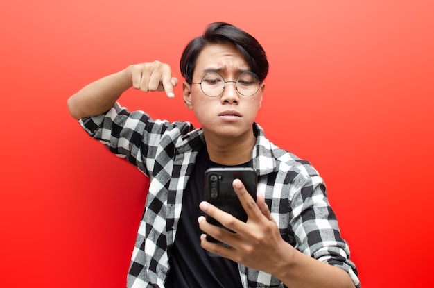 Young asian man holding phone in various expression sad, happy,\
shocked, angry isolated over red.