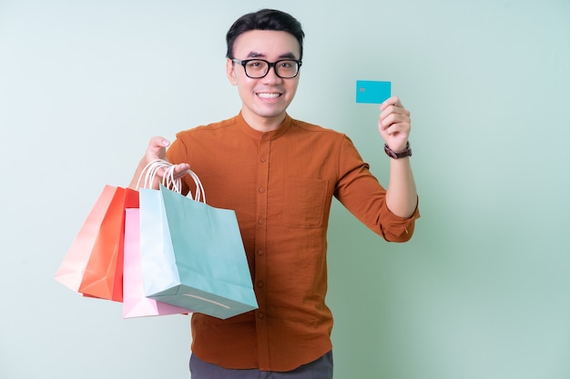 Young Asian man holding shopping bag on green background