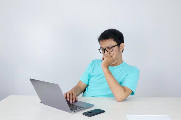 Young Asian Man is Lazy and tired with sleep when working in the front of Laptop Indonesian man wearing blue shirt