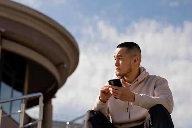 アジア人男性が外で電話を持って座っています 男性は雲の空に背を向けて座っています... 続きを読む →