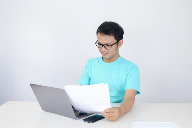 Young Asian Man is smile and happy when working on a laptop and document on hand Indonesian man wearing blue shirt