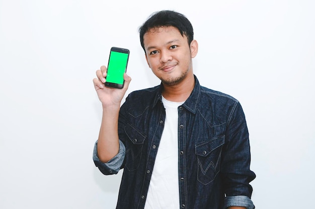 Young Asian man is standing and smiling pointing on green screen on smartphone screen on white background