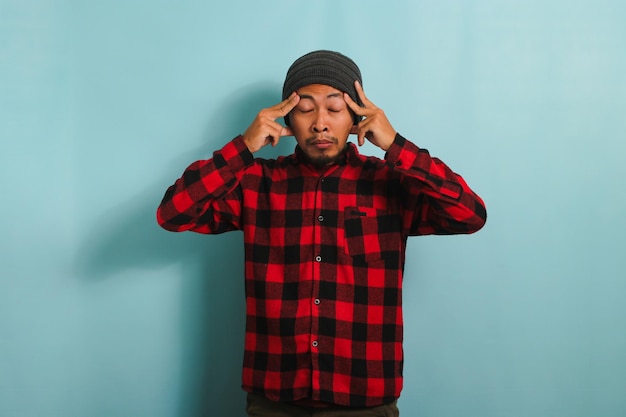 Young asian man is suffering from a headache feeling stressed migraine isolated on blue background