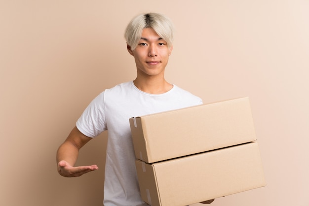 Young asian man over isolated background holding a box to move it to another site