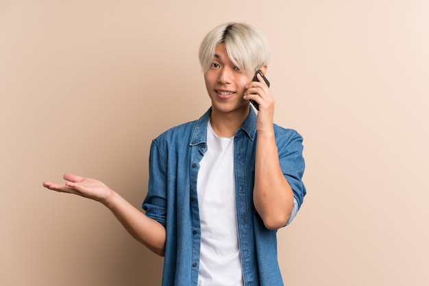 Young asian man over isolated background keeping a conversation with the mobile phone with someone