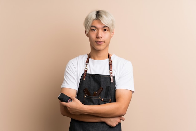 Young asian man over isolated  with hairdresser or barber dress and holding hair cutting machine