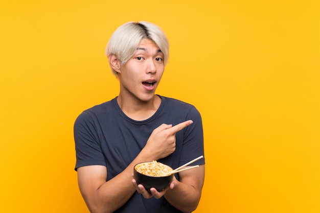 Young asian man over isolated yellow surprised and pointing side