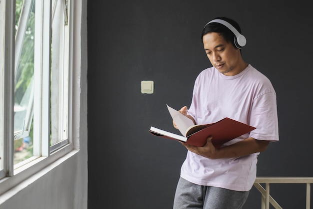 Giovane asiatico che ascolta musica con le cuffie e legge un libro a casa