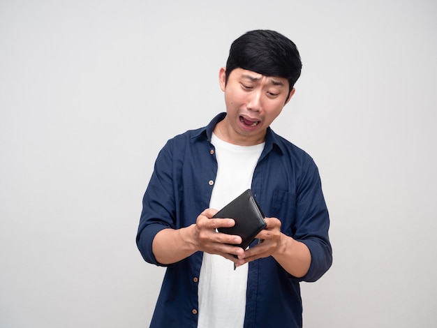 Молодой азиатский мужчина заглядывает в свой бумажник, но без денег чувствует себя шокированным