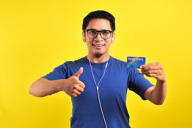 Young Asian man love his debit card, isolated on yellow background