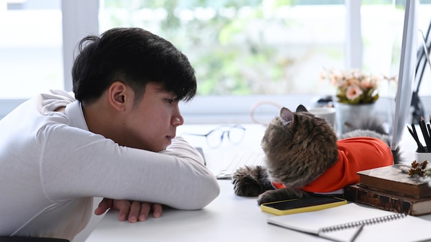 Young Asian man lying on white desk with his cat at home