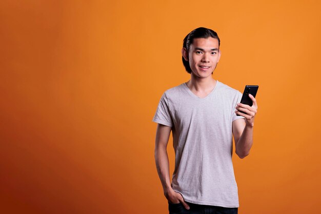 ソーシャル メディアを使用して、スマートフォンでメッセージングを行う若いアジア人男性。肯定的な表情で立っている陽気なティーンエイ ジャー、携帯電話でインターネットを閲覧、オンライン コミュニケーションの概念