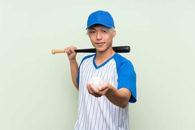 Young asian man playing baseball over isolated green 