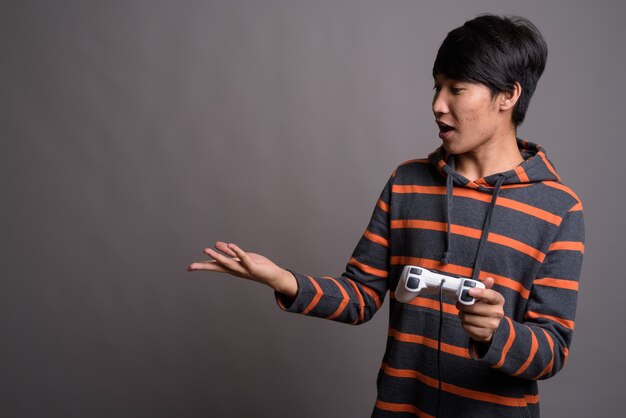 Young Asian man playing games against gray wall