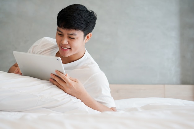 young asian man playing tablet on bed in weekend