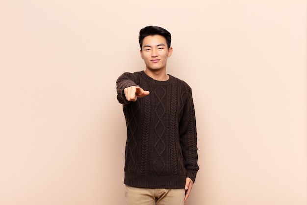 Young asian man pointing at camera with a satisfied, confident, friendly smile, choosing you over color wall