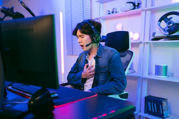 Photo young asian man professional gamer sits on a chair and grabs his chest suffering heart attack