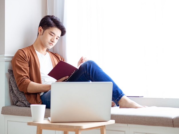 Young asian man reading a book while relaxing at home