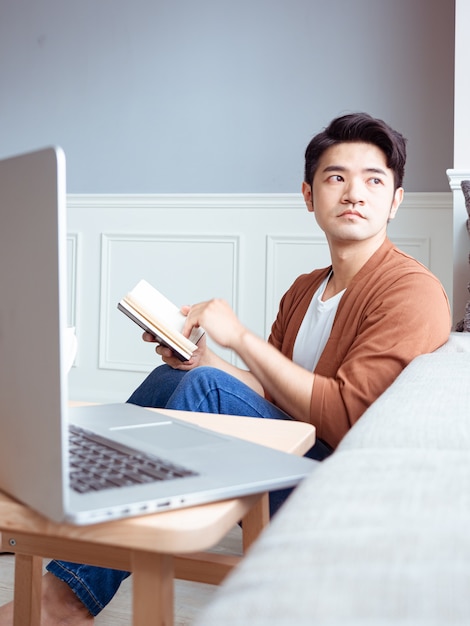 Young asian man reading a book while relaxing at home