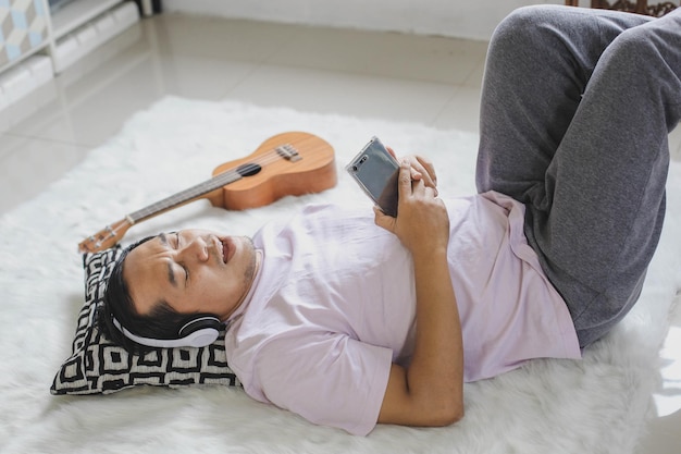 Молодой азиатский мужчина расслабляющий, лежа, счастливо поет в квартире