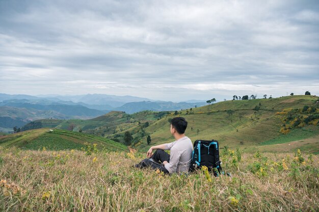 Young asian man relaxing with camera bag on farmland hill in rural