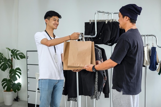 Молодой азиатский мужчина обслуживает покупателя в магазине одежды