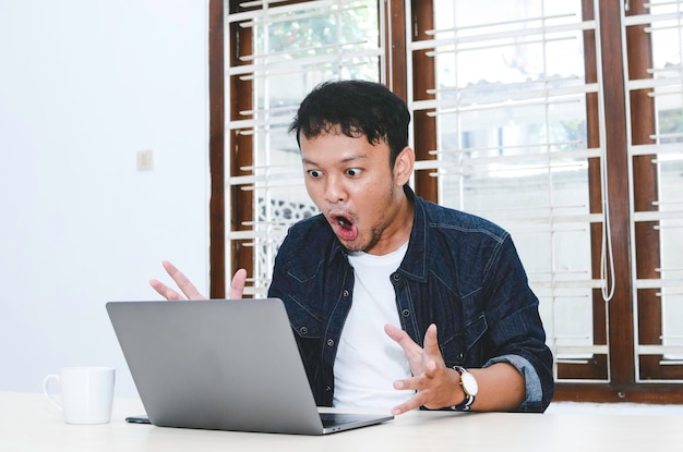 Young Asian man shocked and wow what he see in the laptop