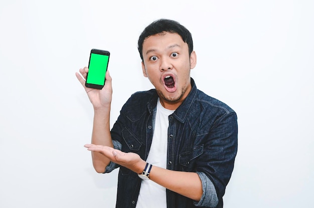 Young asian man shocked and wow with showing green screen and pointing smartphone