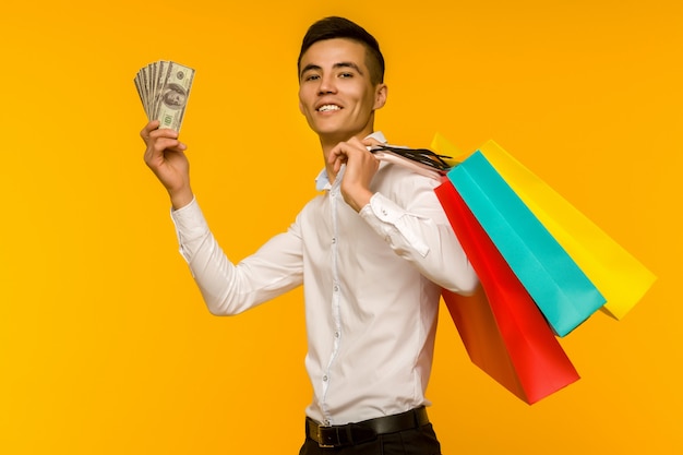 Young asian man showing his shopping bag and money on yellow background