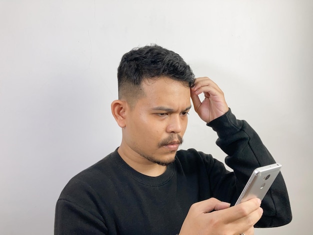 a young asian man shows confused face while looking at bad news on cellphone