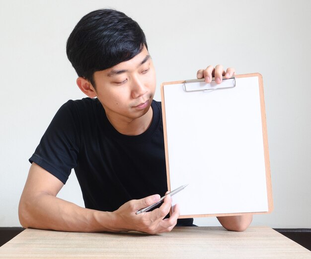 사진 젊은 아시아 남자는 책상에 앉아 빈 문서비즈니스 개념에서 클립보드가 펜을 가리킵니다.