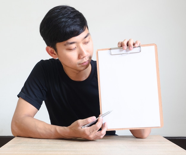 Young Asian man sit at the desk and show clipboard point the pen at blank documentBusiness concept