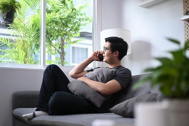 Young Asian man sitting on couch and talking on mobile phone