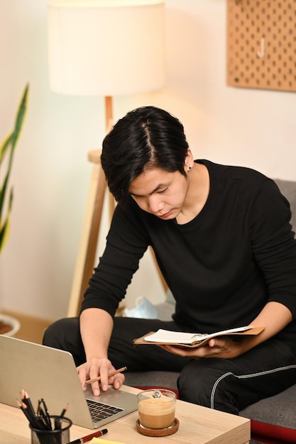 Young Asian man sitting on couch and using laptop