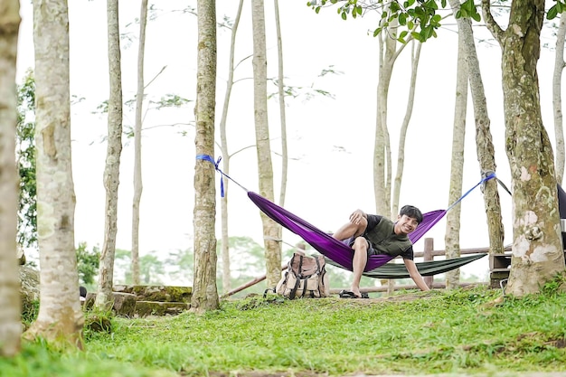 Young asian man sitting relaxed in hammock enjoying fresh nature